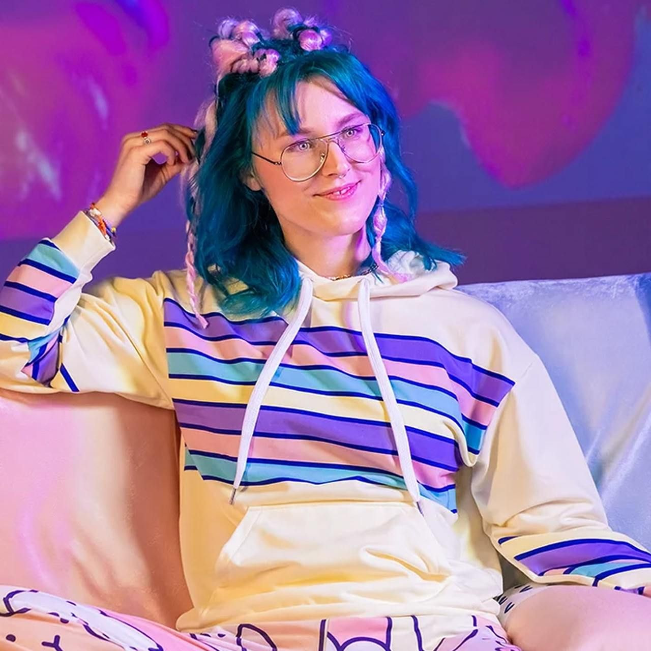 A woman is sitting on a couch and wearing a white all-over-print hoodie with colorful lines.